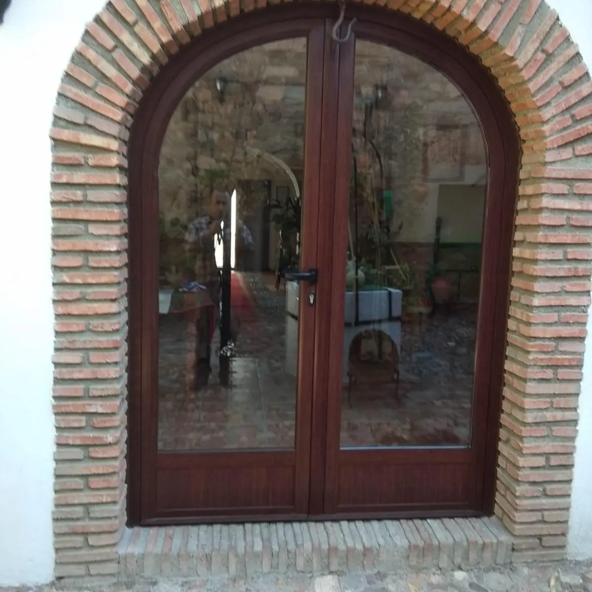 Puerta de dos hojas con arco de medio punto imitación madera en hueco de ladrillo visto